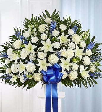 White floral standing spray with blue accents and a blue ribbon