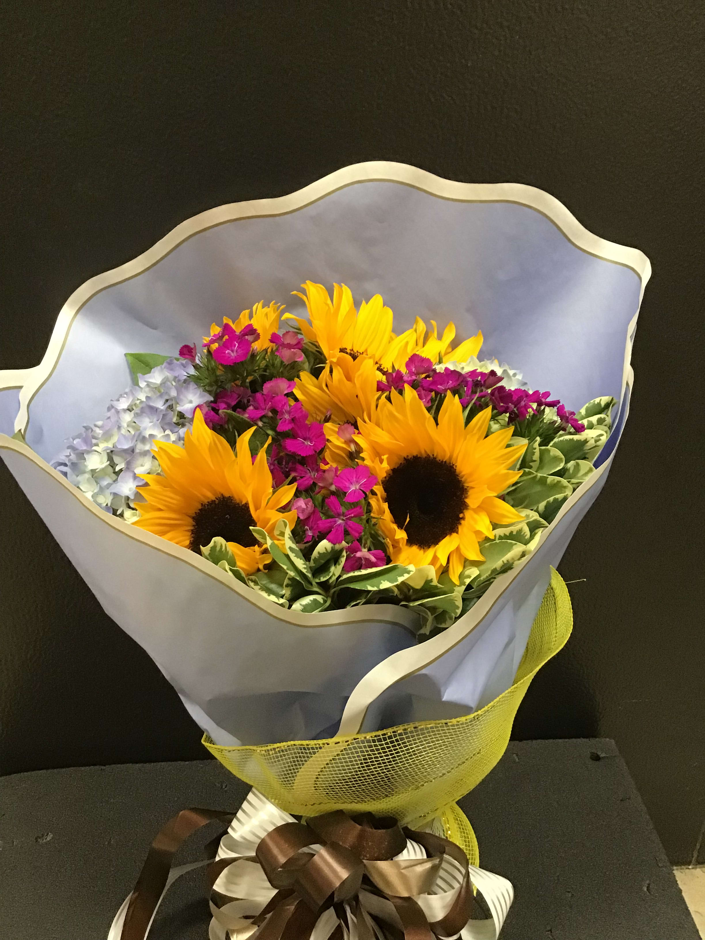 Bouquet of sunflowers and small purple flowers wrapped in pale paper