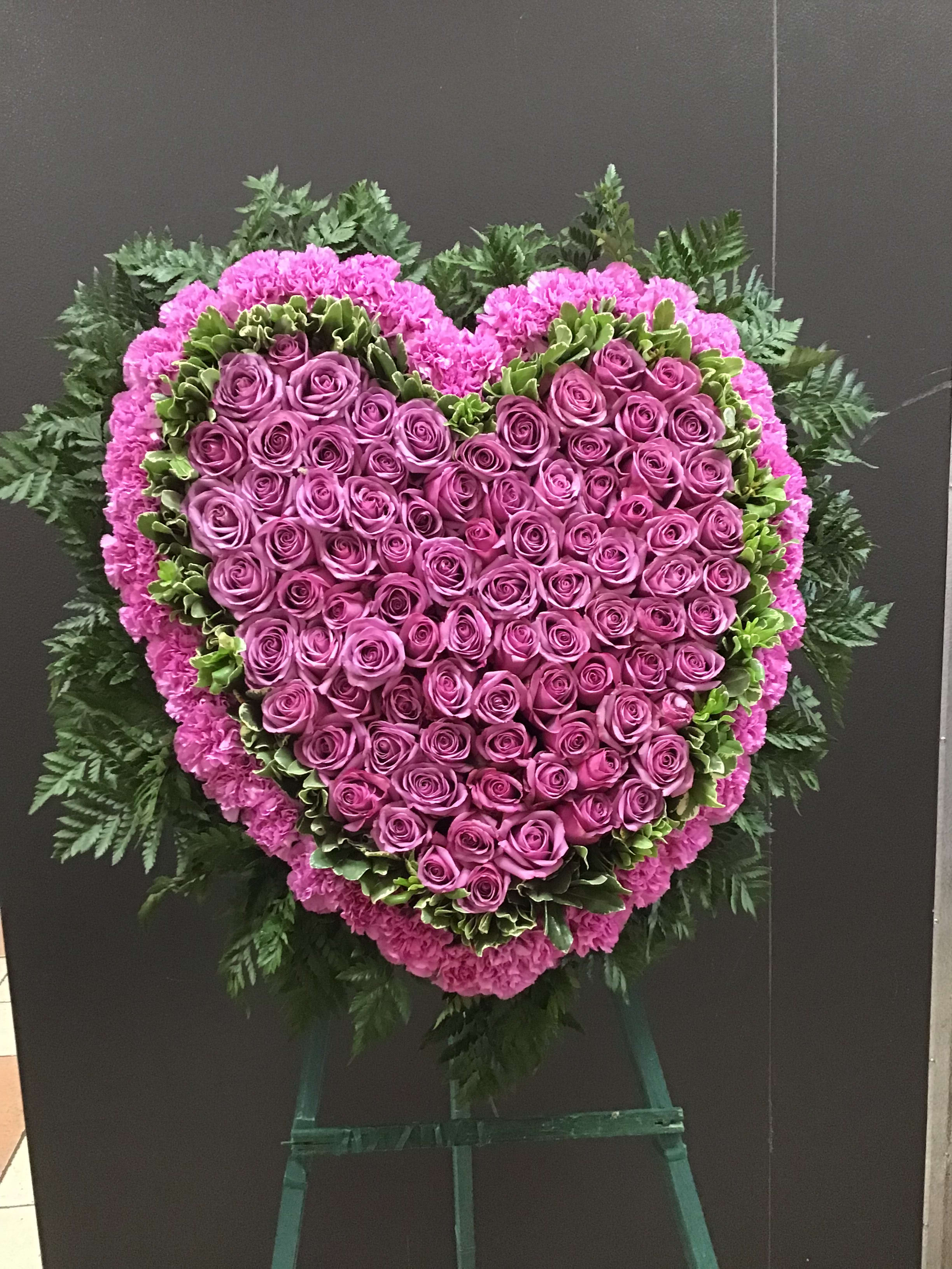 Heart-shaped pink rose funeral spray on an easel
