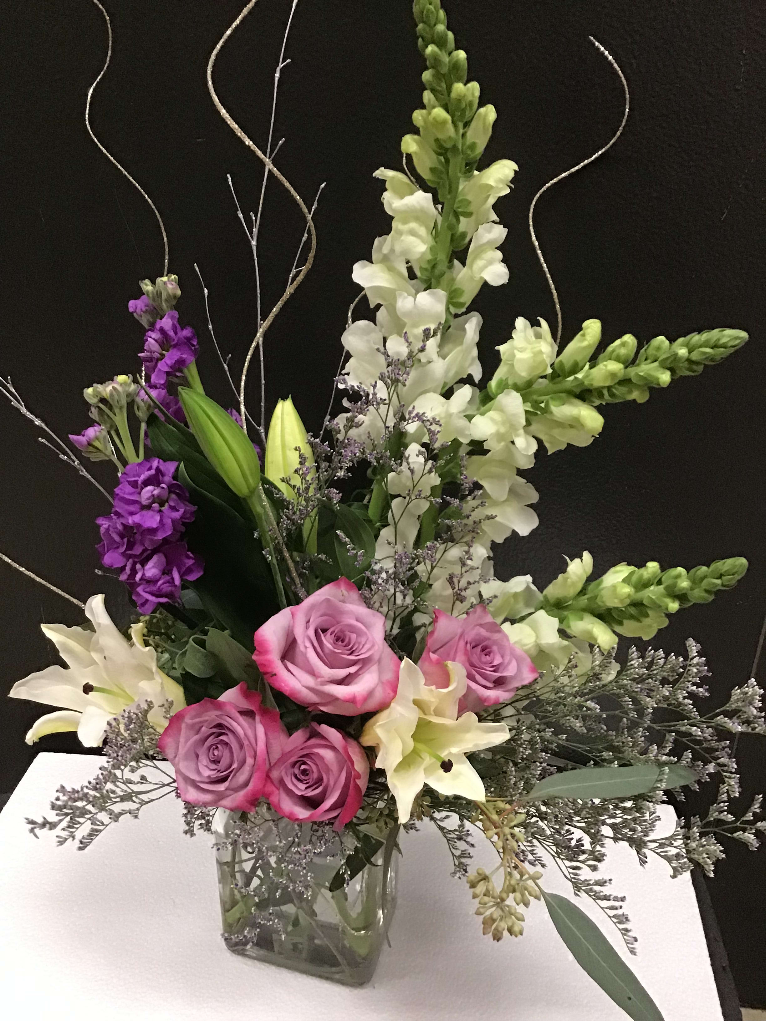 Mixed bouquet of pink roses, white lilies, and purple snapdragons in a glass vase