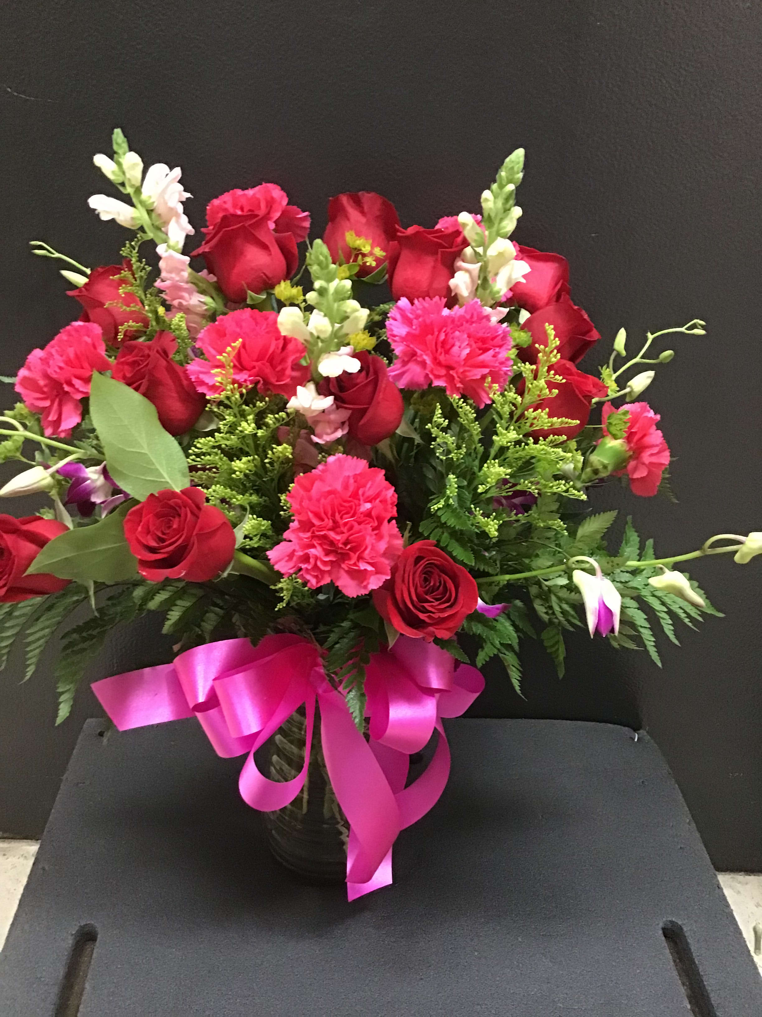 Red roses and pink carnations in a vase with a pink ribbon