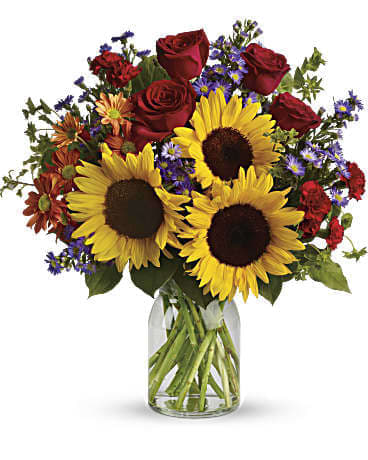 Bouquet of sunflowers, red roses, and purple flowers in a glass vase