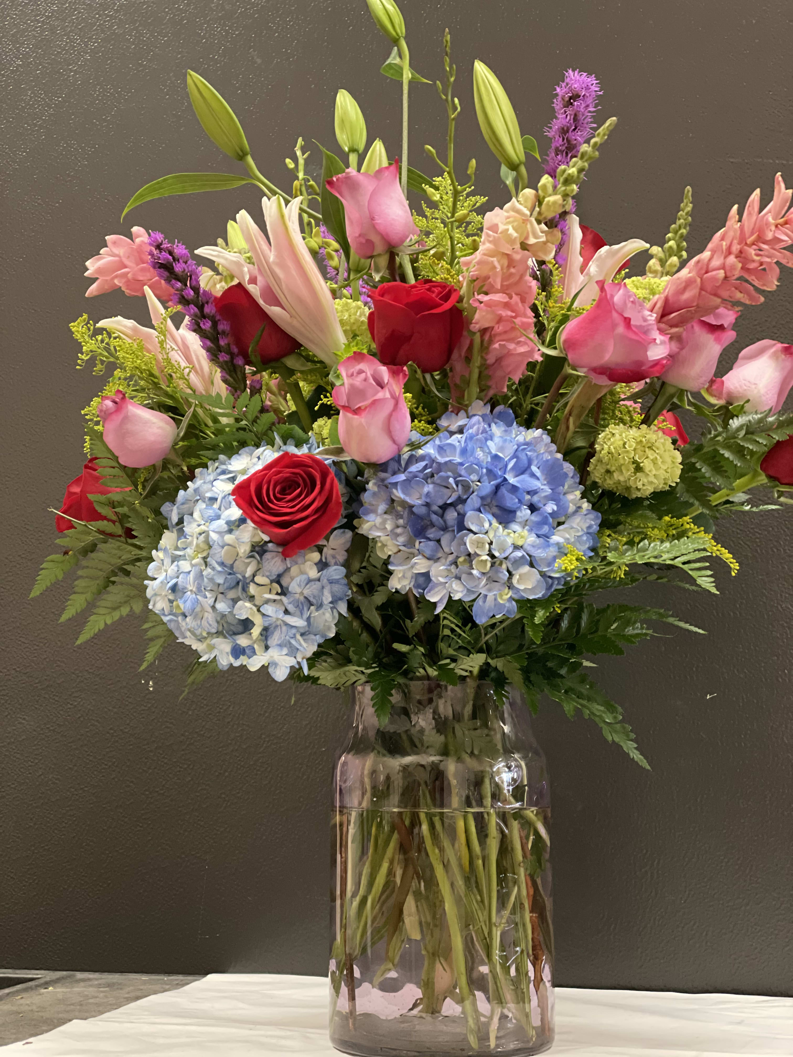 Mixed bouquet of roses, lilies, hydrangeas, and pink blooms in a glass vase