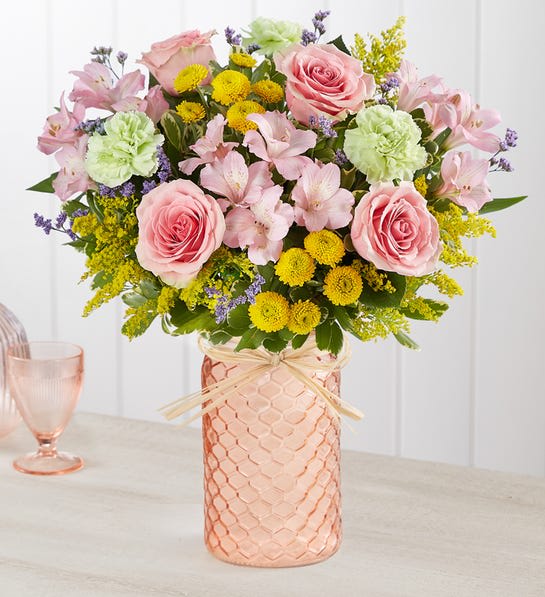 Pastel Posy -  Our new peach quartz mason jar, creating the perfect complement of color. From the soft floral tones to the charming honeycomb container design, it’s a gift full of warmth and happiness. All-around arrangement with pink roses and Peruvian lilies (alstroemeria), yellow button poms, lime green carnations and purple limonium; accented with assorted greenery