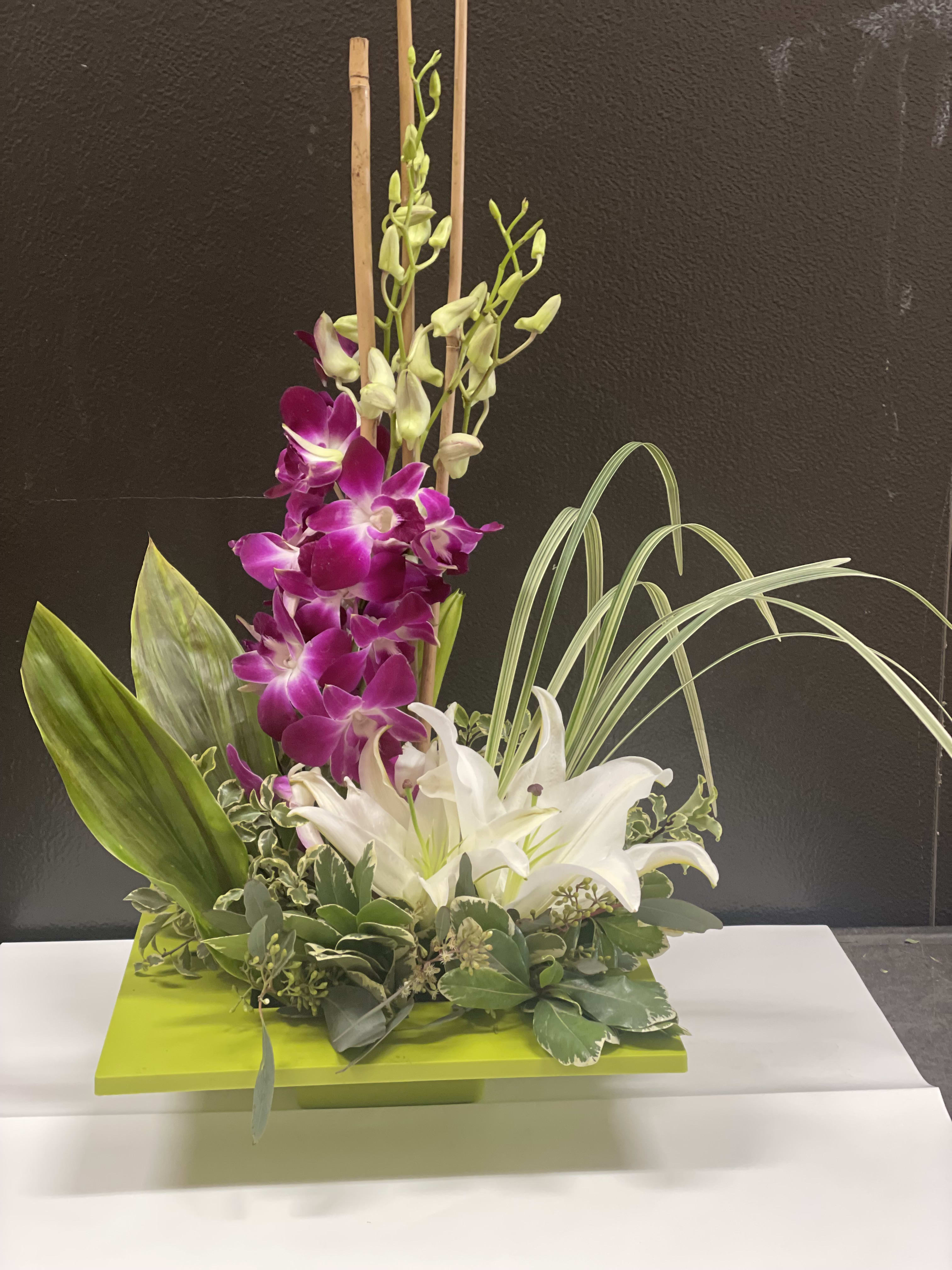Purple and white orchids arranged in a low green container