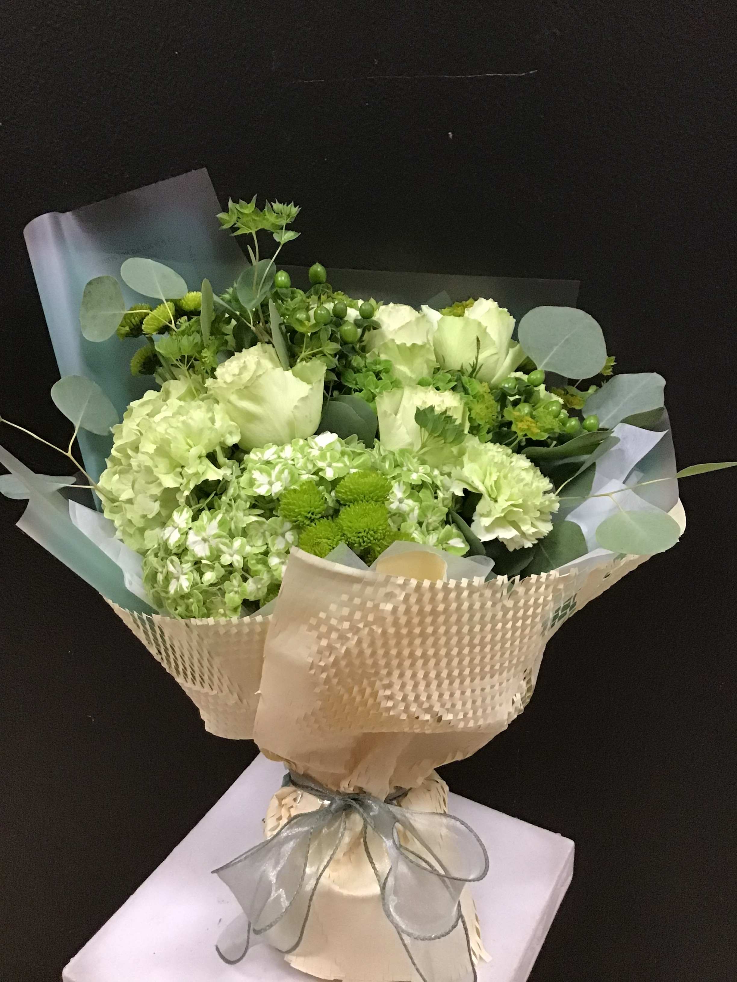 Green and white bouquet wrapped in beige paper with a ribbon