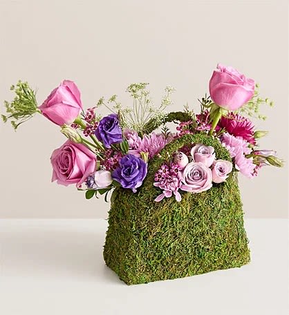 Avignon Lavender -  This arrangement made with purple and lavender roses and other blooms all but overflow from a planter shaped like a handbag and clad in preserved moss.  