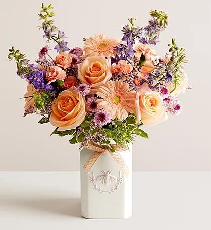 Peach roses and purple flowers in a white vase
