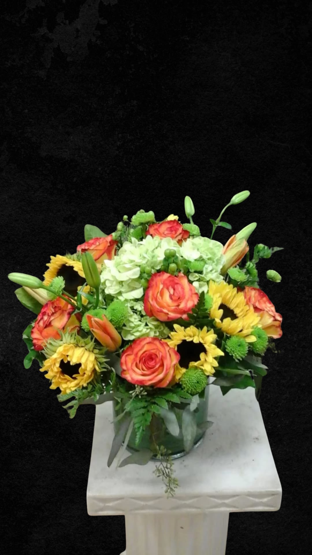 Bouquet of orange roses, yellow sunflowers, and white hydrangeas in a glass vase