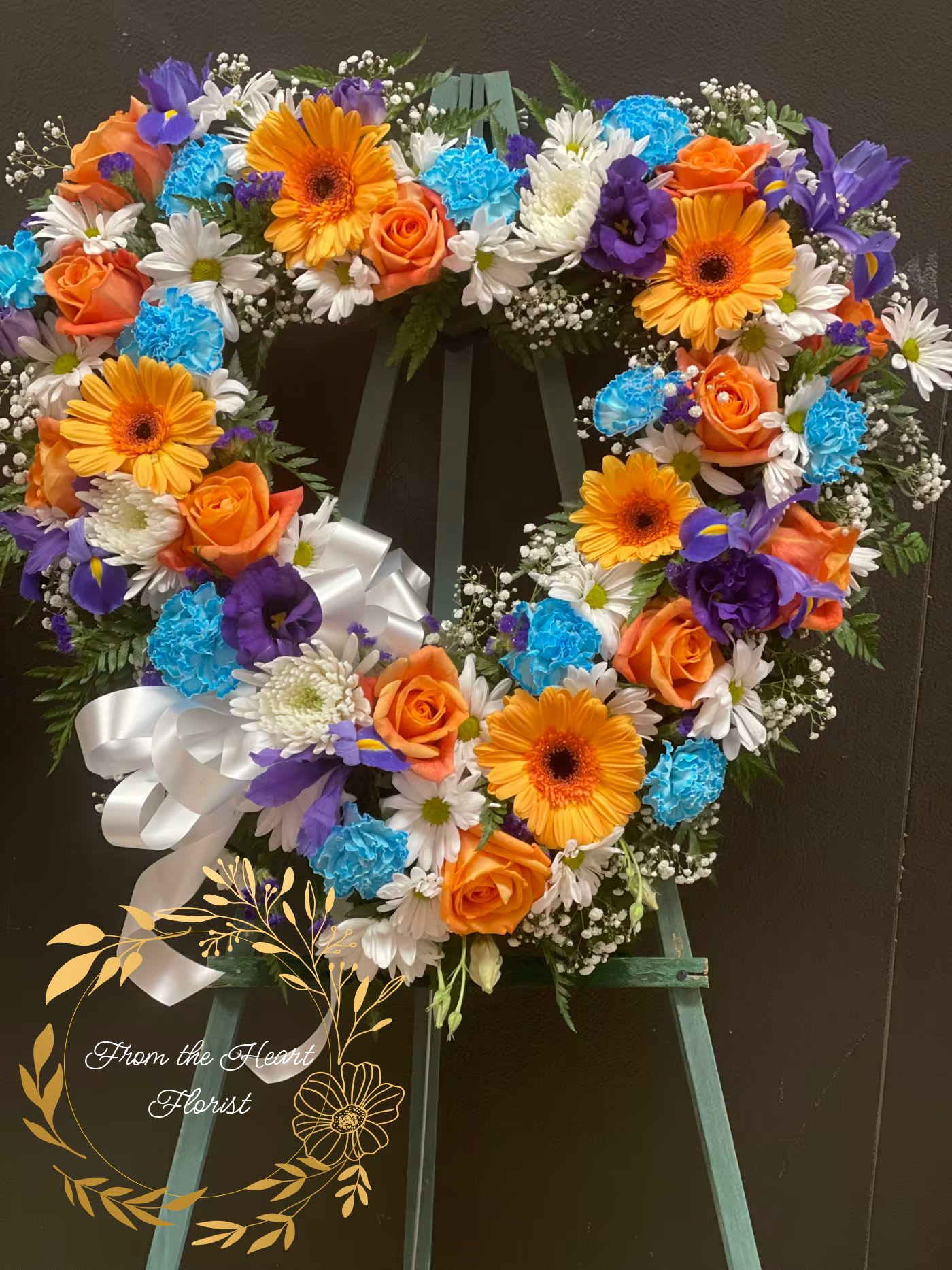 Heart-shaped floral wreath with orange roses, gerbera daisies, and blue carnations