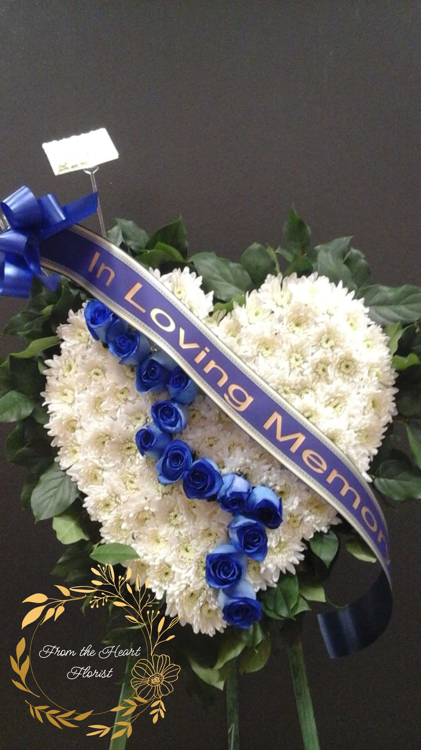 Heart-shaped white flower arrangement with blue roses and a ribbon