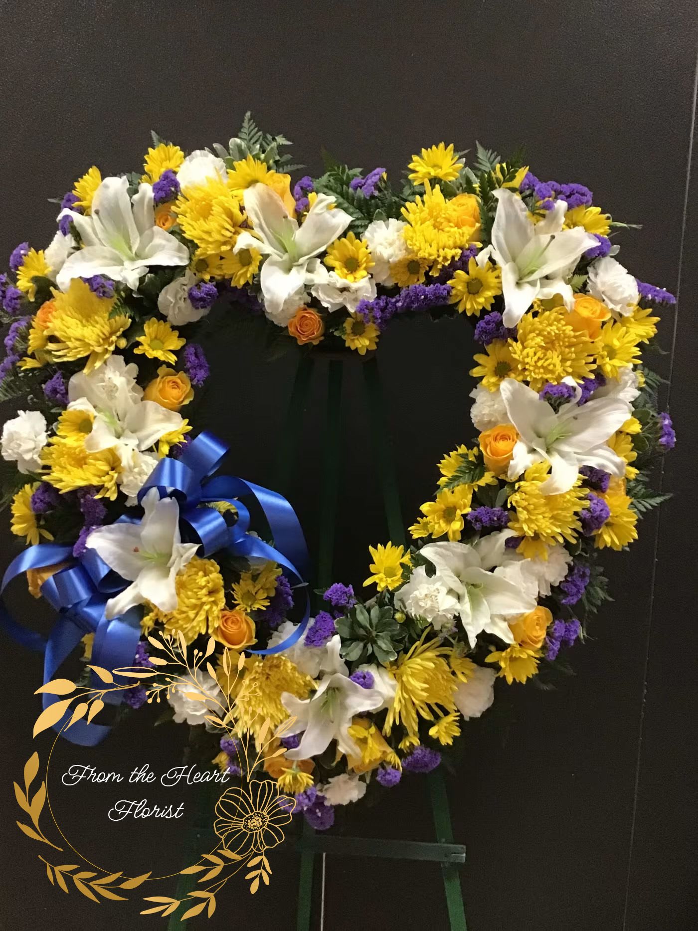 Heart-shaped floral wreath with white lilies, yellow blooms, and purple accents