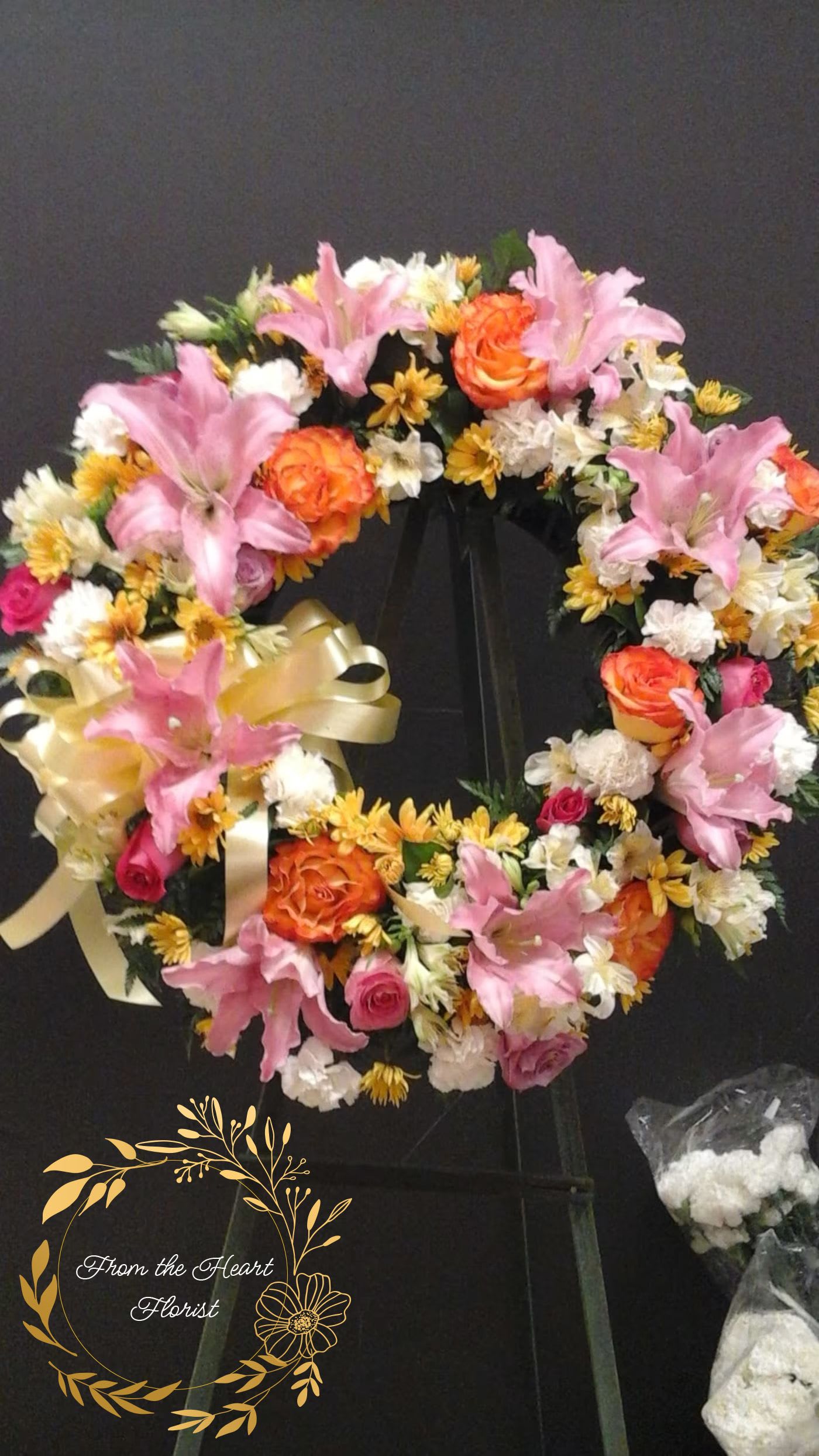 Heart-shaped floral wreath with pink lilies, orange roses, and white daisies