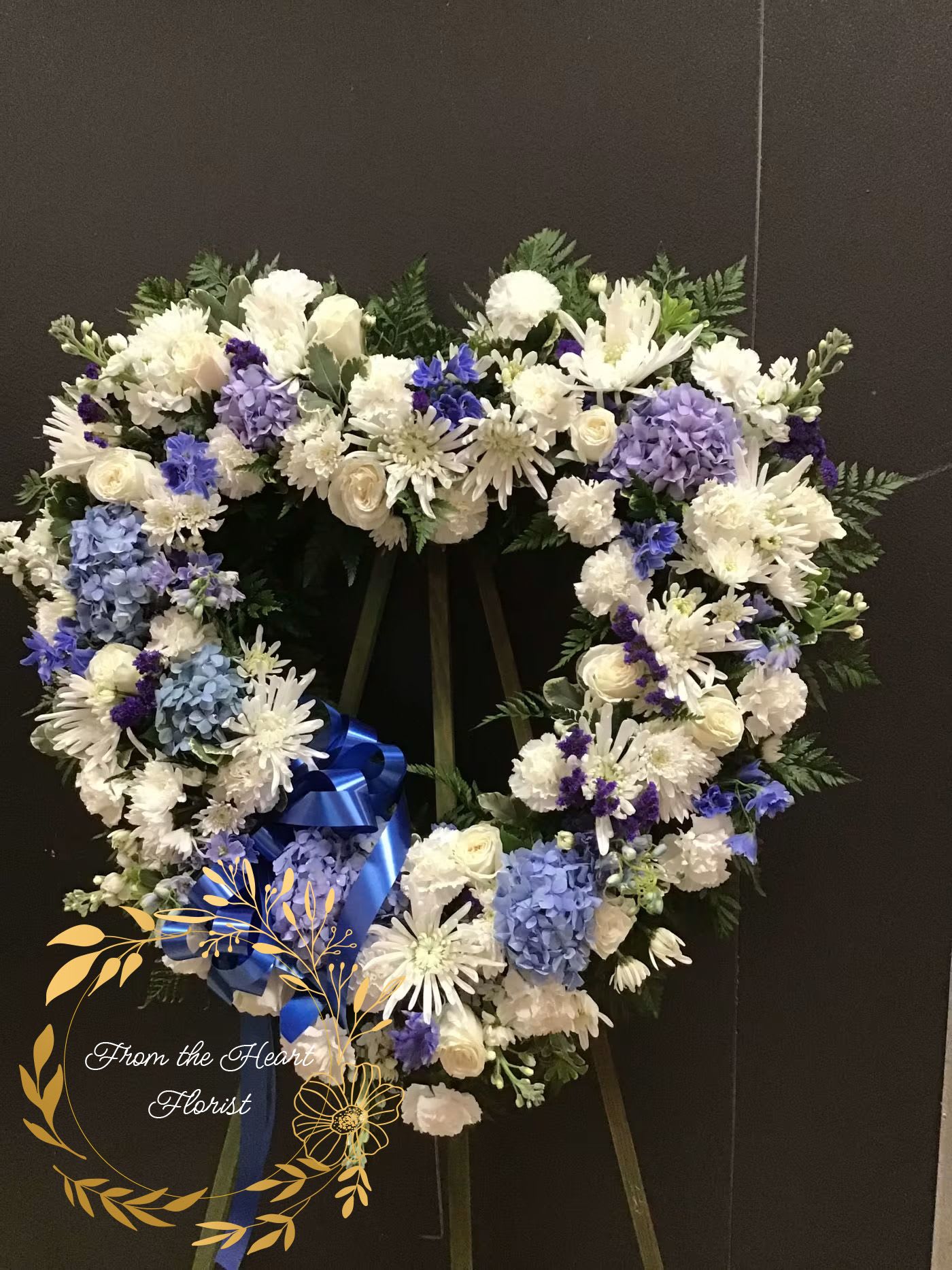 Heart-shaped white and blue floral wreath on an easel with a blue ribbon