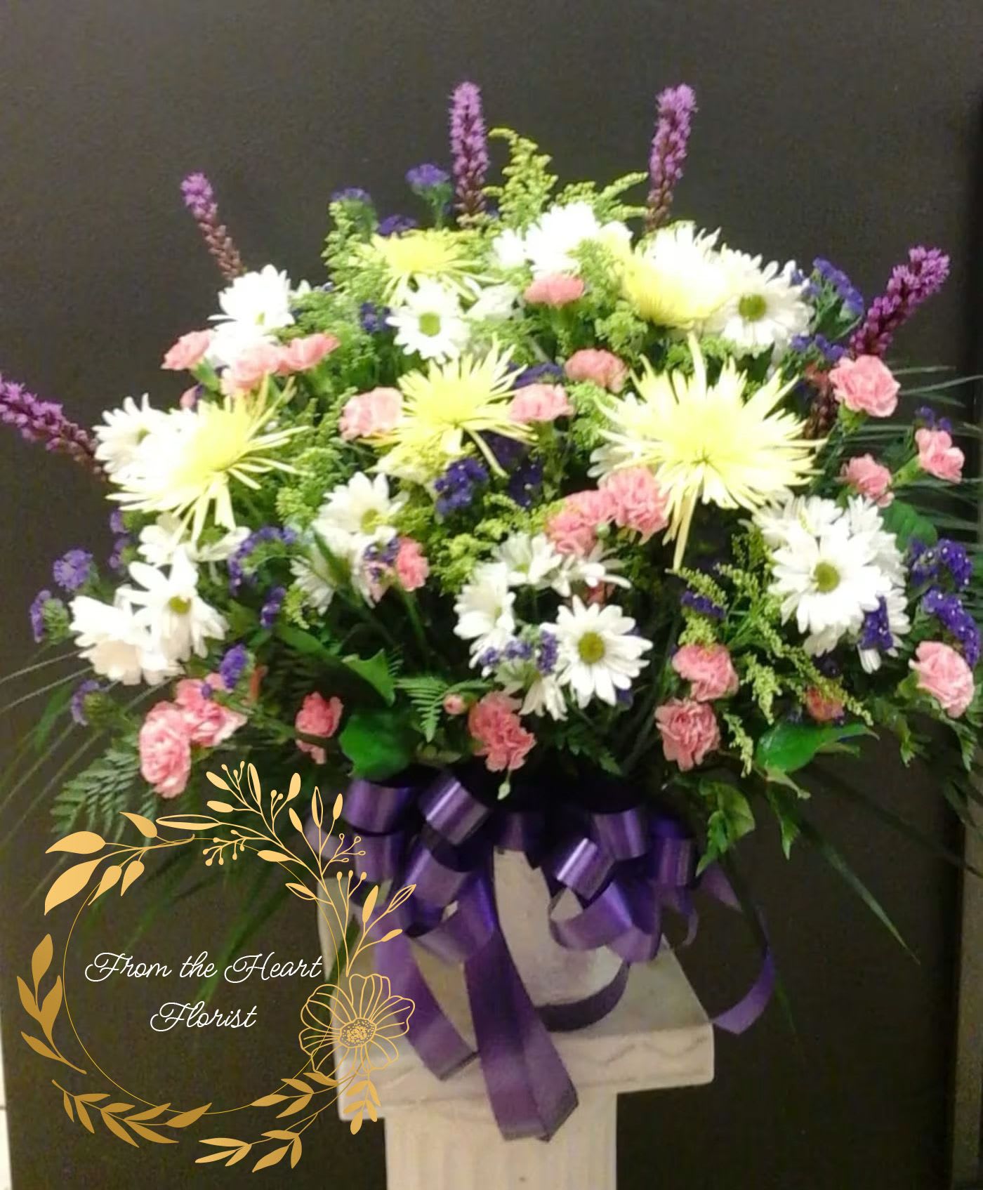 Large mixed flower arrangement with purple ribbon on a pedestal
