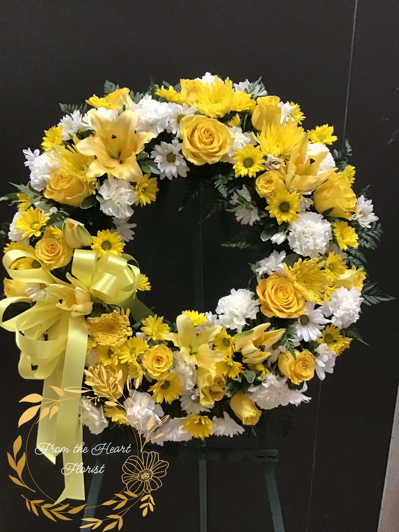 Yellow and white floral wreath with a ribbon bow on a dark stand