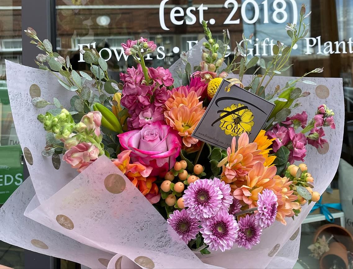 Mixed bouquet with pink roses, orange dahlias, and purple daisies in polka-dot wrap