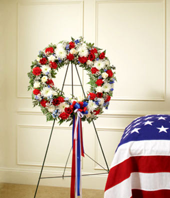 Red, white, and blue floral wreath on a stand with ribbon streamers