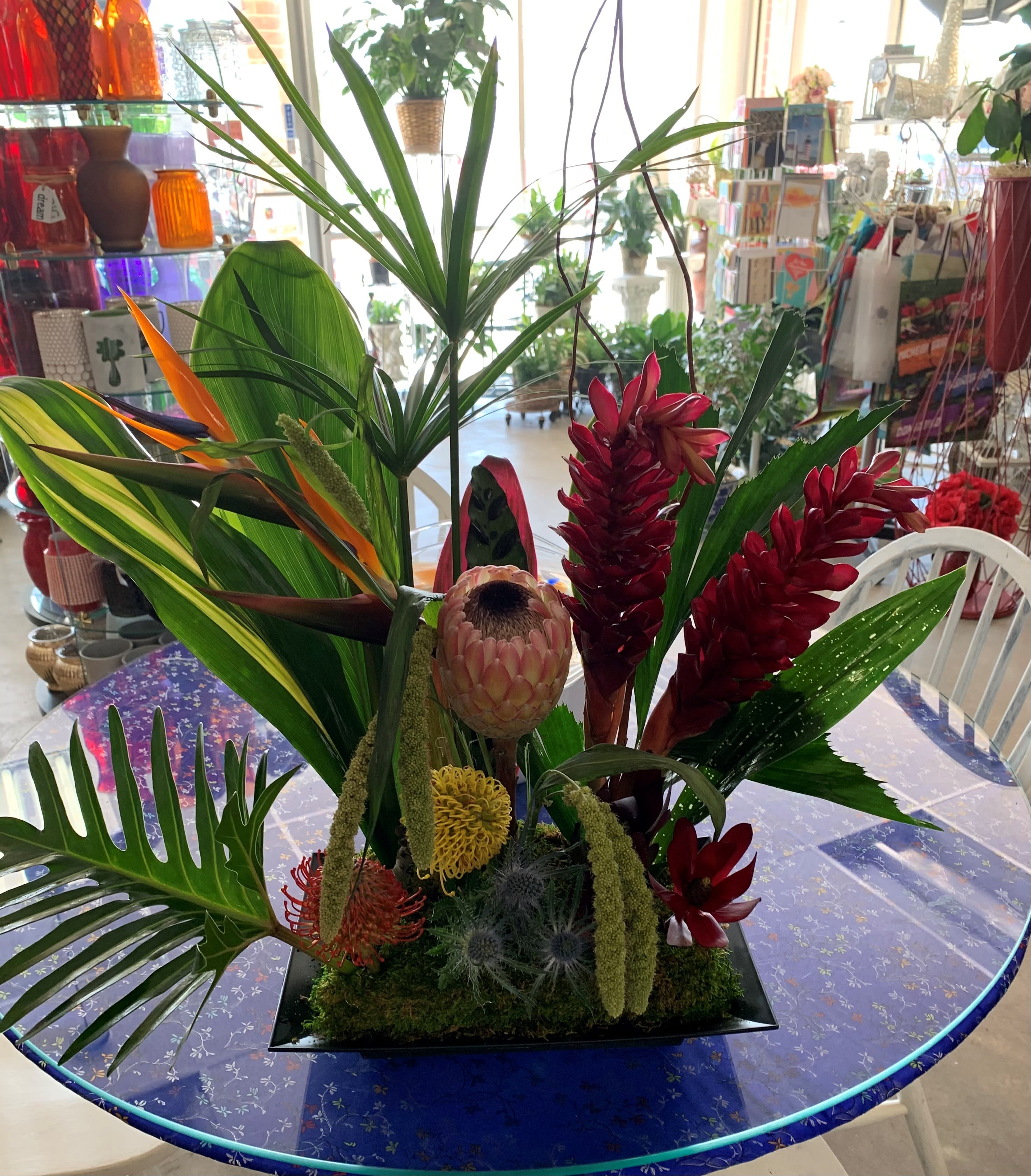 Tropical floral arrangement with red blooms and large green leaves in a black vase