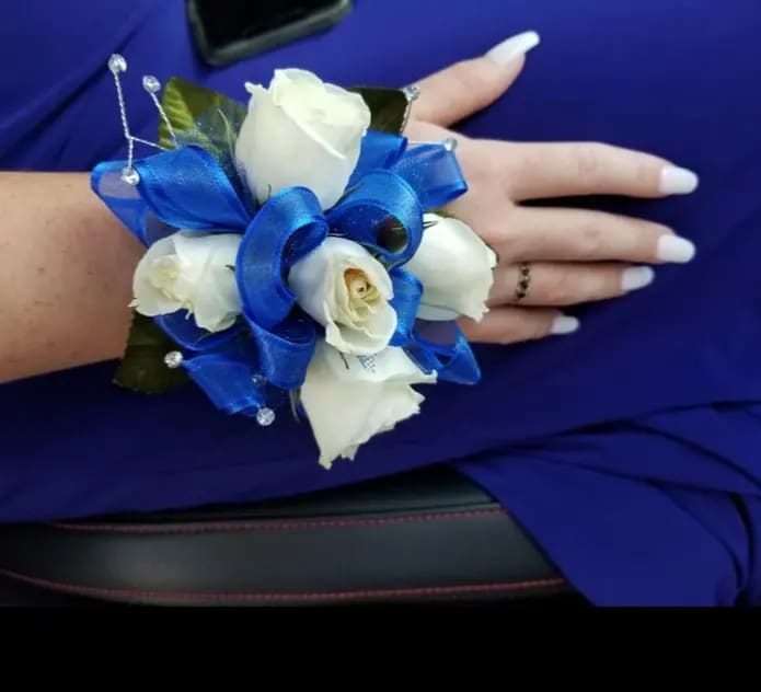 White rose wrist corsage with bright blue ribbon on a person's wrist