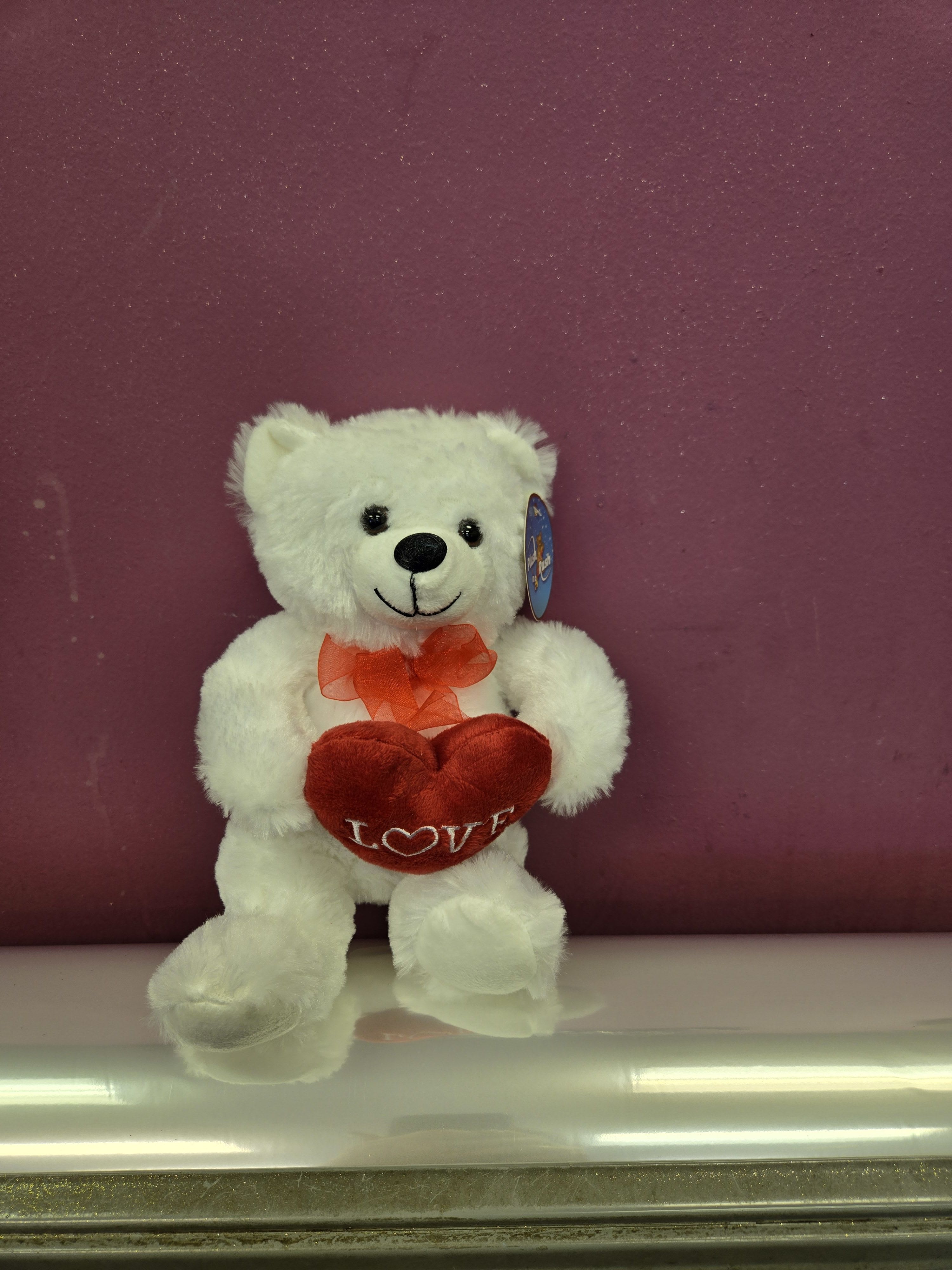 White teddy bear holding a red heart with a ribbon