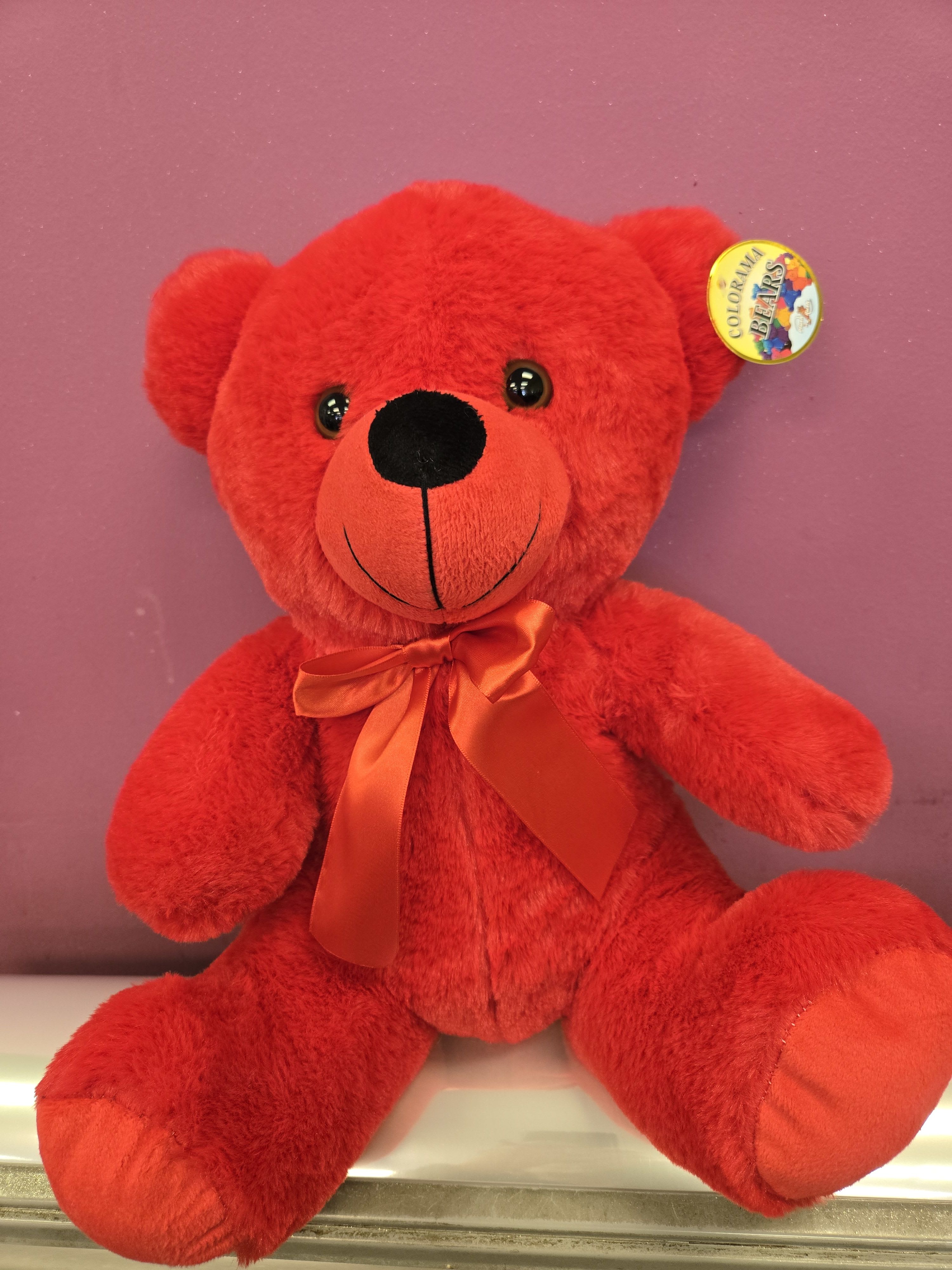 Bright red teddy bear with satin bow sitting against a purple background