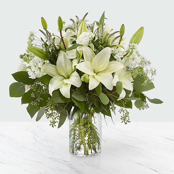 The FTD Alluring Elegance Bouquet - Our Alluring Elegance Bouquet is a striking array of ivory and green within a clear textured glass vase. Handcrafted using Asiatic lilies interwoven with white Veronica white stock Queen Anne’s lace silver dollar eucalyptus and seeded eucalyptus this bouquet graces every room with a touch of elegance. GOOD bouquet is approx. 17"H x 14"W. BETTER bouquet is approx. 18"H x 17"W. BEST bouquet is approx. 19"H x 18"W.