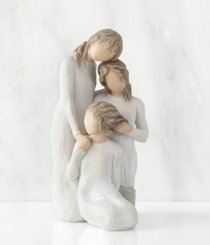 Three faceless figurines in white clothing posed closely together