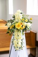 Standing cross-shaped arrangement of white and yellow flowers on an easel in a church aisle