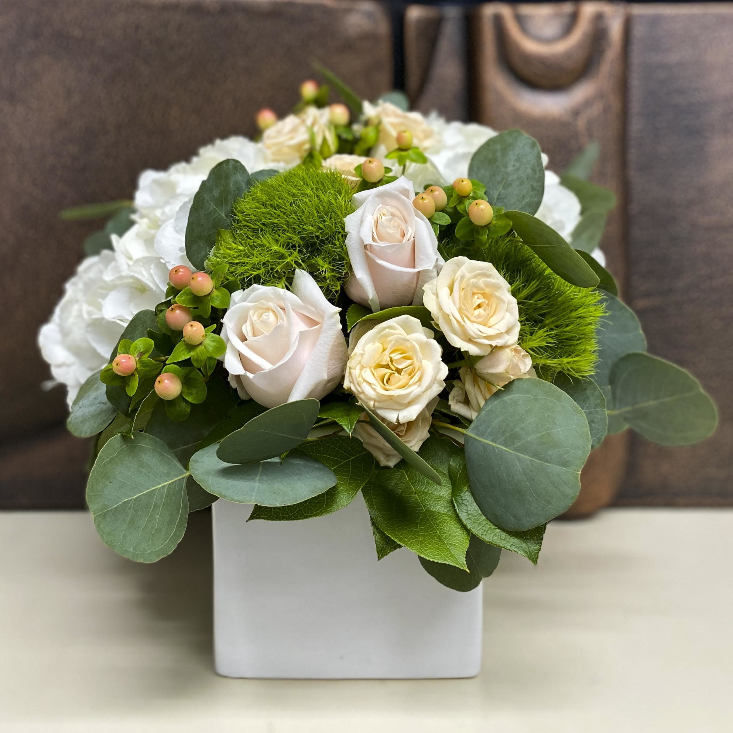 White roses and green pom-pom flowers in a white square vase