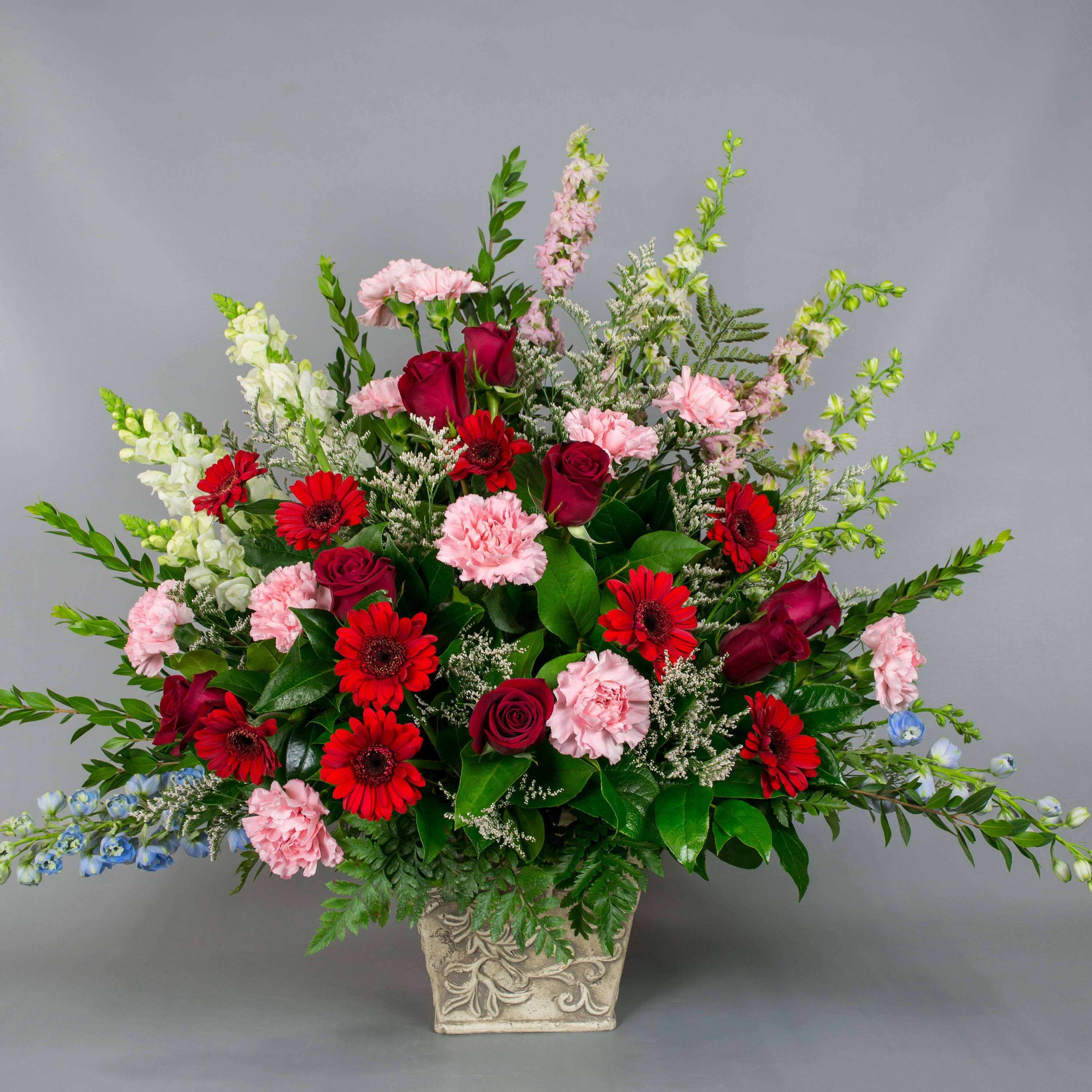 Mixed bouquet of red roses, pink carnations, and red daisies in a decorative vase