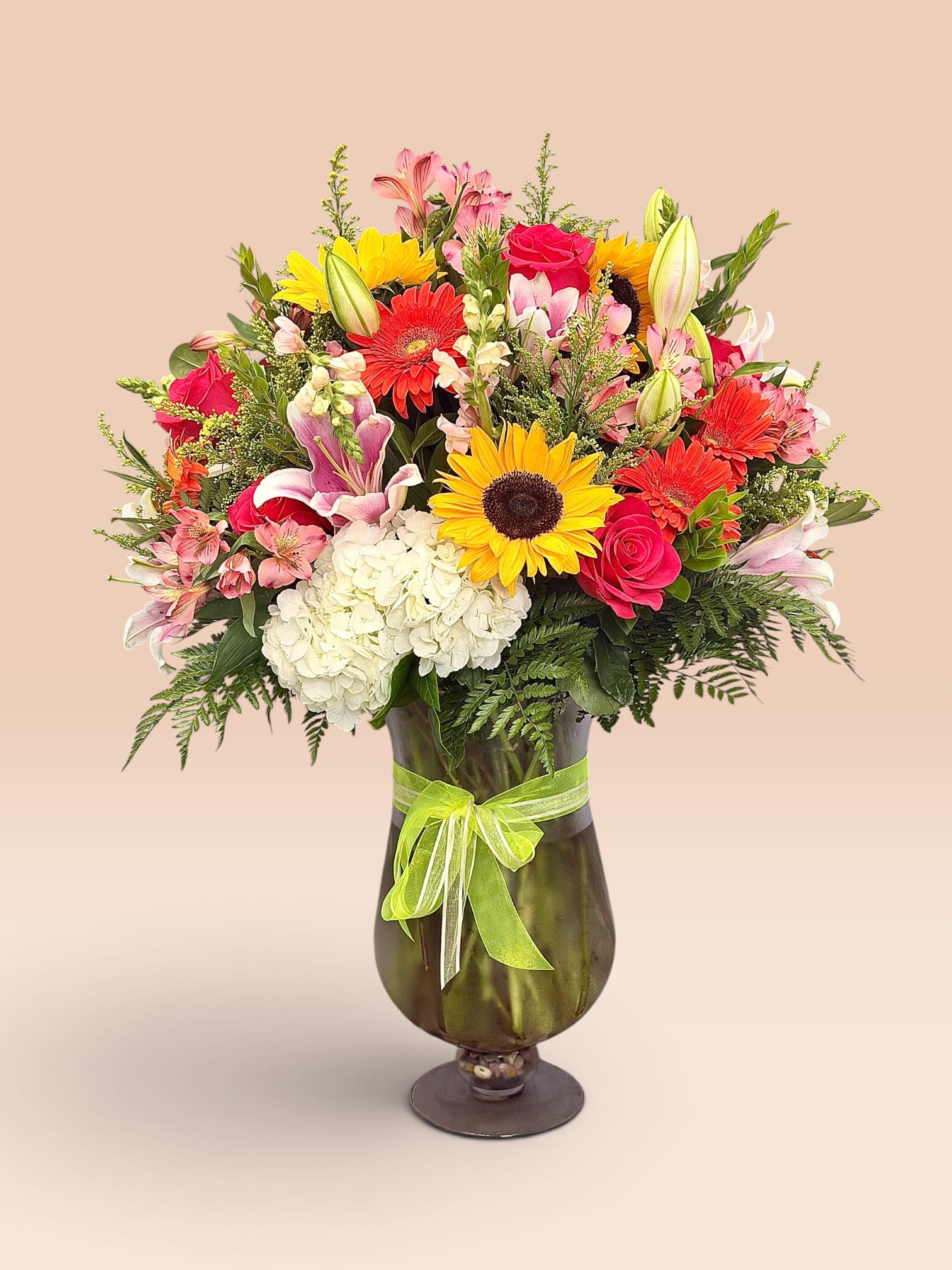 Mixed bouquet of roses, lilies, sunflowers, and gerbera daisies in a glass vase