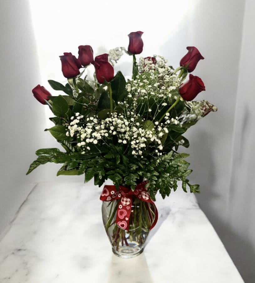 Red roses in a glass vase with baby's breath and a heart ribbon