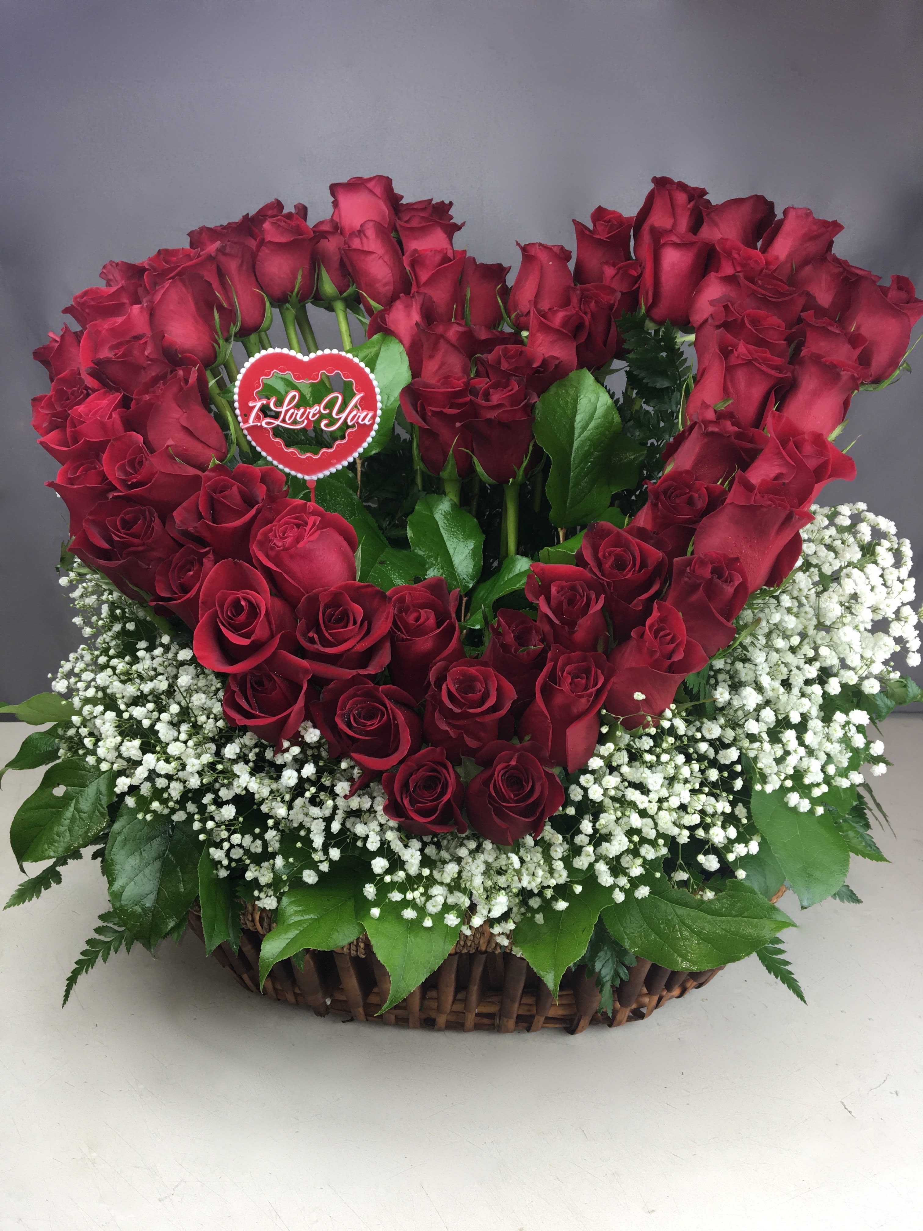 Heart-shaped red rose arrangement in a wicker basket with baby's breath