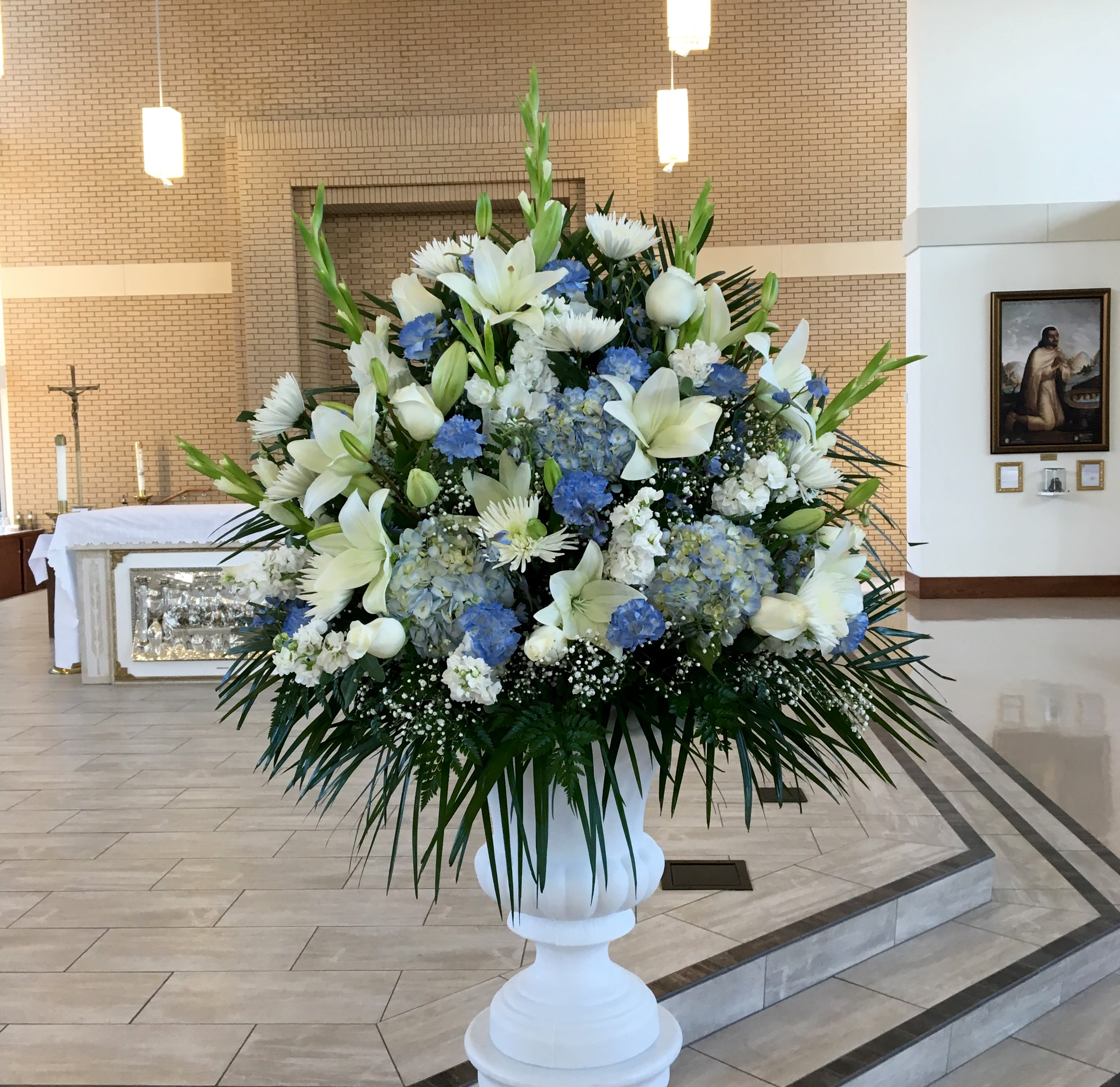 Large white and blue floral arrangement in a white pedestal vase