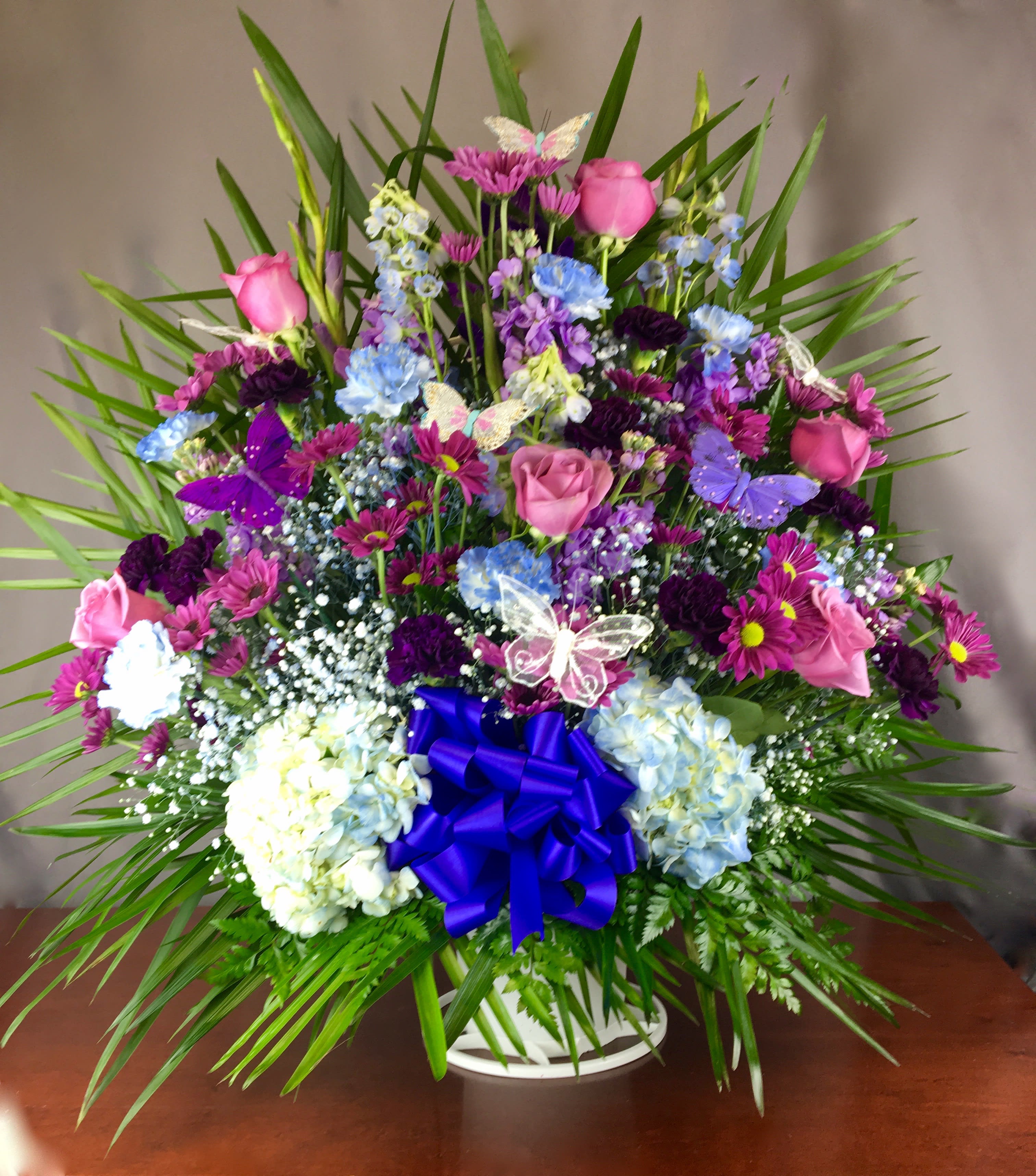 Colorful mixed flower arrangement in a white basket with a blue bow