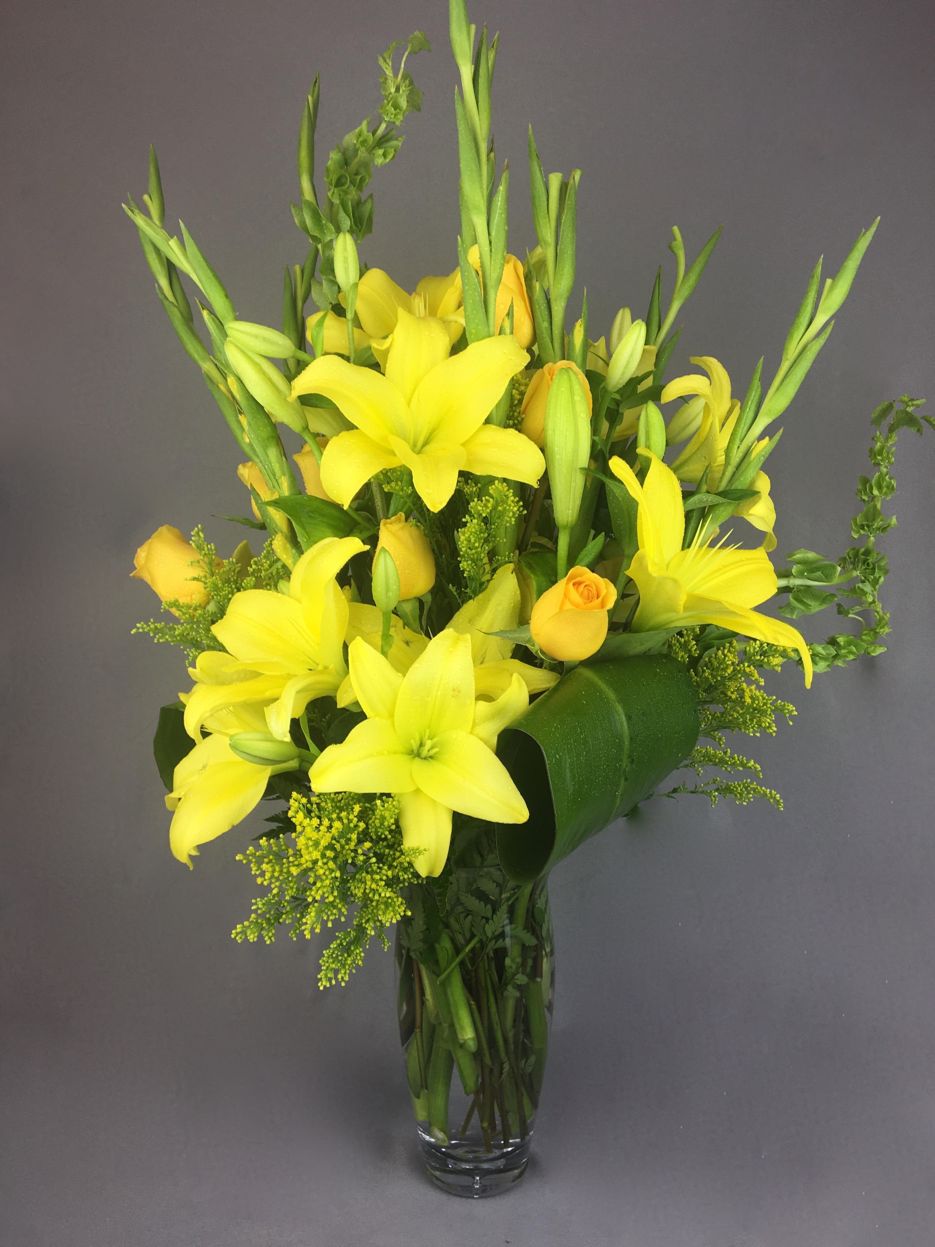 Yellow lilies and roses arranged in a clear glass vase