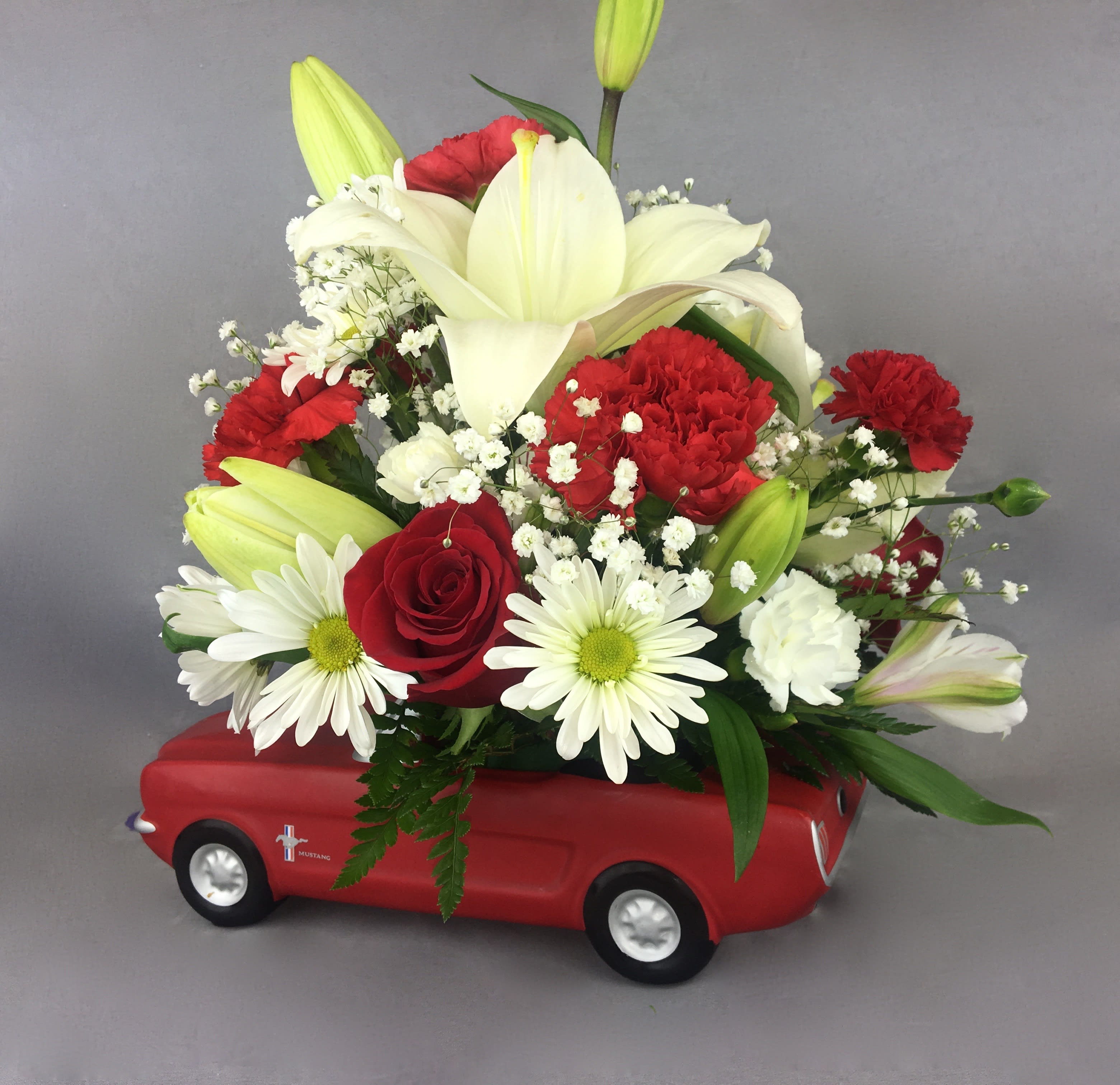 Red and white flower arrangement in a red toy car container