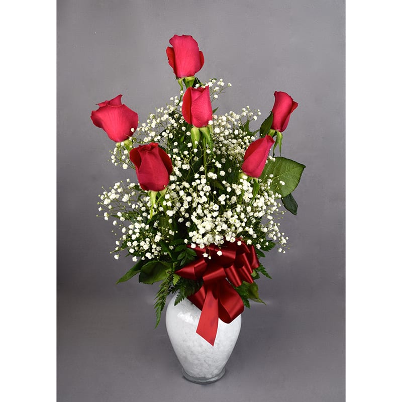 Red roses arranged in a white vase with baby's breath and a red ribbon
