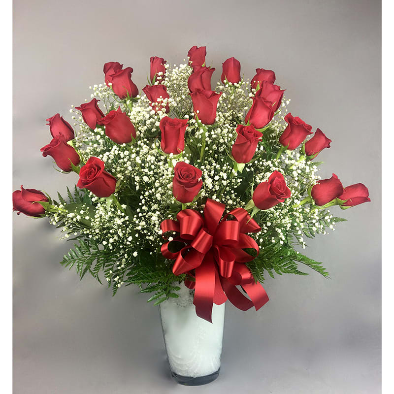 Red roses arranged in a clear vase with a red ribbon bow