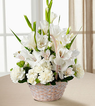 White floral arrangement in a woven basket with tall green leaves