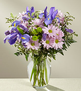 Purple irises and pink daisies in a clear glass vase
