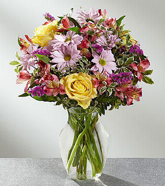 Mixed bouquet of yellow roses, pink daisies, and alstroemeria in a clear vase