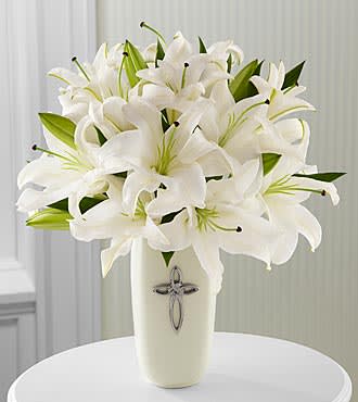 White lilies arranged in a tall cream vase with a silver cross emblem