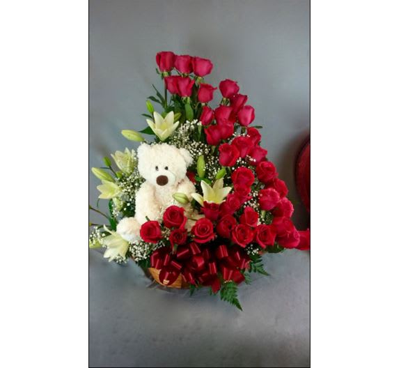 Red roses and white lilies arranged with a teddy bear in a basket