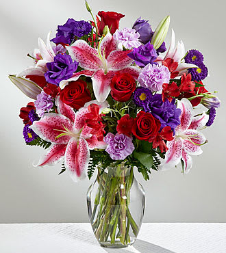 Bouquet of red roses, pink lilies, and purple flowers in a glass vase