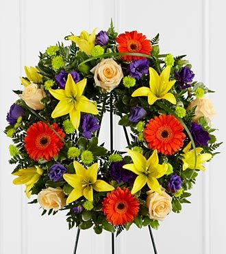 Circular floral wreath with yellow lilies, orange gerberas, and cream roses