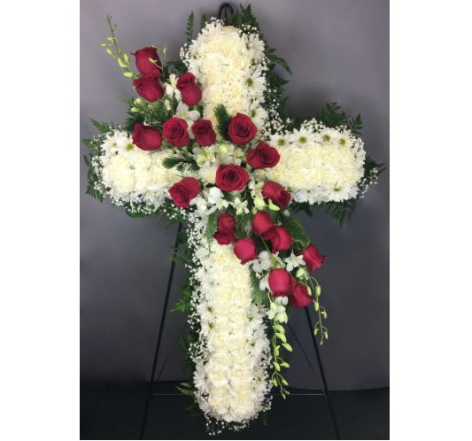 Cross-shaped floral arrangement with red roses and white flowers on an easel