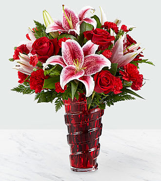 Red roses and pink lilies arranged in a red glass vase