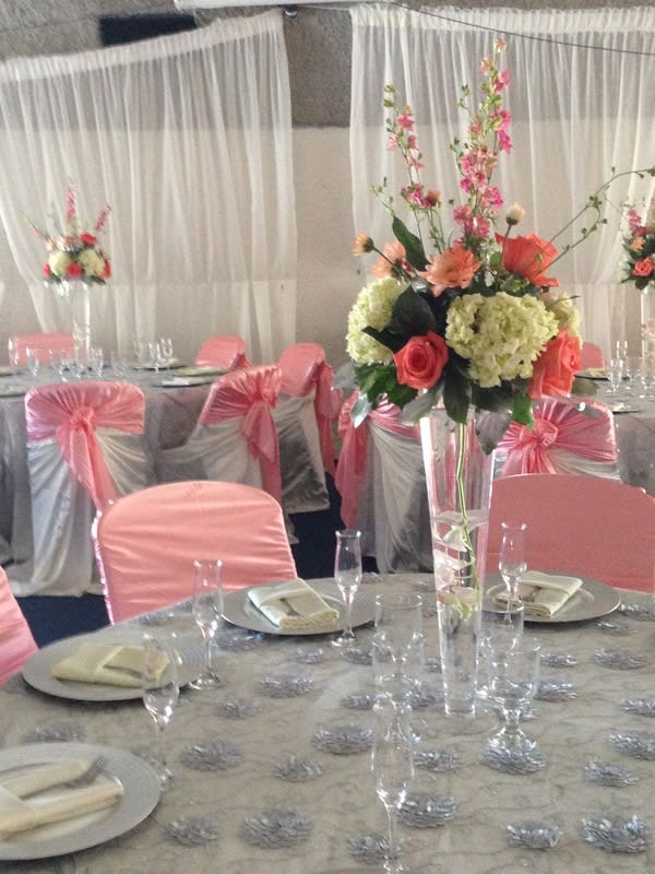 Tall floral centerpiece with pink and coral flowers in a clear vase at a decorated banquet table